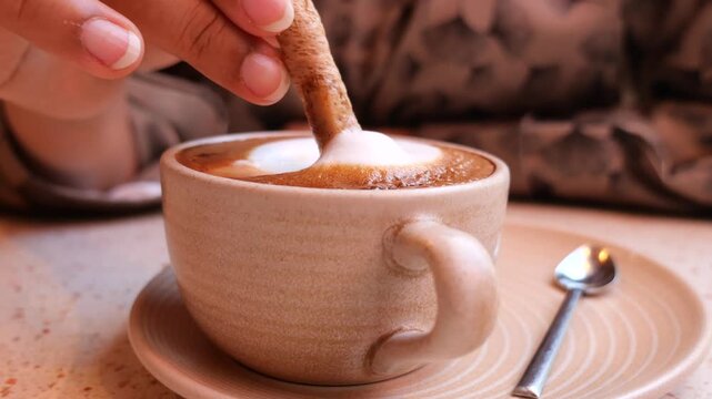 Person Dipping a Wafer Cookie into a Cup of Cappuccino