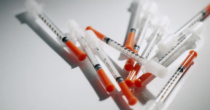 Large quantity of disposable insulin syringes with orange caps lying in a pile, slowly rotating on a clean white background, highlighting the concept of diabetes management and healthcare