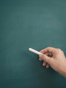 Childs hand holding white chalk against a blank green chalkboard ready for writing or drawing.