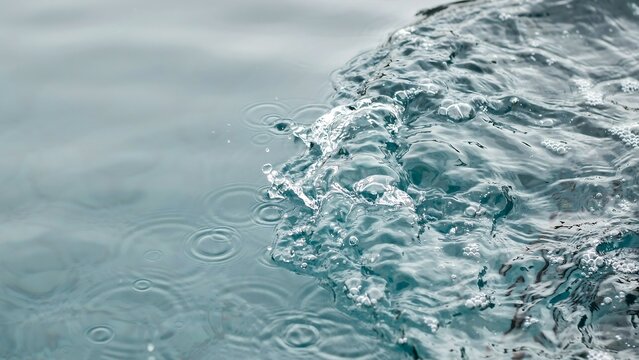 Rain drops falling on a calm water surface creating circular ripples with flowing water