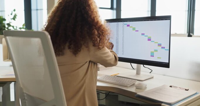 Businesswoman manager using computer spreadsheet in office. Screen shows a project schedule with tasks on a timeline, supporting data planning and analysis. Key concept is project planning.