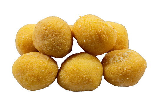 A pile of round, yellow indian besan laddu sweets with a textured, granular surface arranged on a dark black background