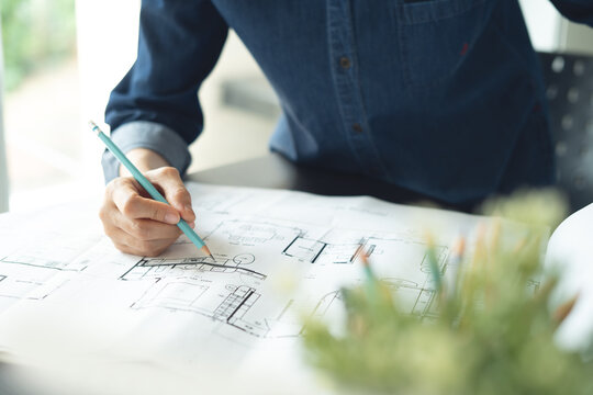 Woman architect working with interior design project with blueprint on table in studio office, close up