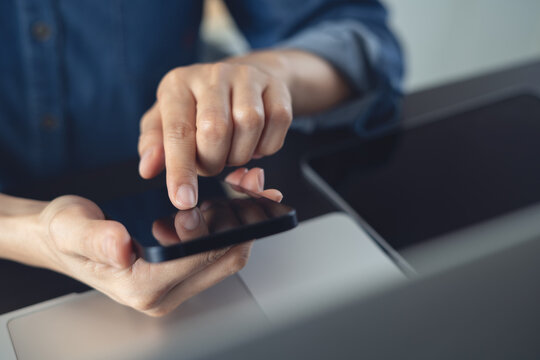 Closeup, woman using smartphone, touching on screen with laptop on desk during working at office