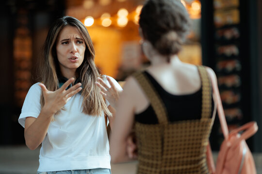 Expressive Young Woman Gesturing During Conversation With Friend Outdoors. Emotional female model explaining something with hand gestures while talking to another girl