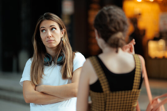 Skeptical Young Woman Listening To Her Friend Outdoors. Anxious or doubtful female looking up while talking with another girl on the street