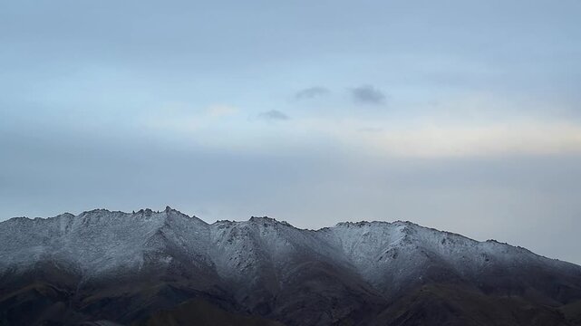 Snow-dusted mountain ridges and rugged peaks under a moody overcast sky in the high-altitude Himalayas.