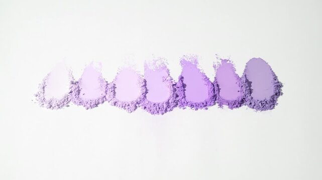 Vertical jib shot of seven violet aligned streaks of loose powder on a subtle grey surface lit by moving light creating dynamic shadows