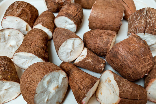 A close-up photo of unpeeled cassava pieces on a white tray.