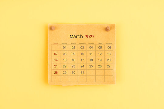 March 2027 brown calendar with wooden thumbtack on yellow background.