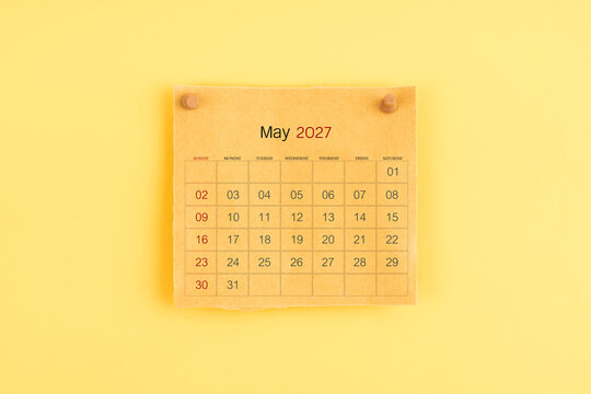 May 2027 brown calendar with wooden thumbtack on yellow background.