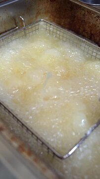 Vertical close up of lowering breaded chicken into a commercial deep fryer with rapidly boiling hot oil