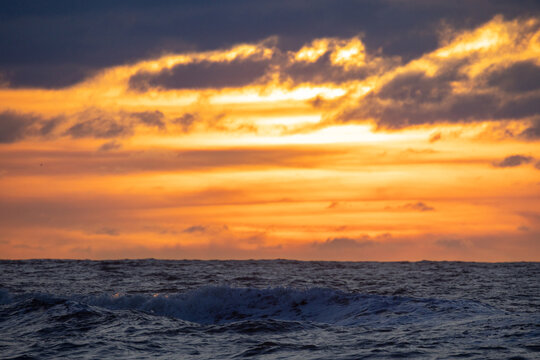 A stunning sunset with vibrant colors reflecting on ocean waves, framed by dramatic clouds, creating enchantment