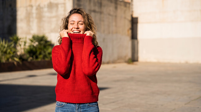 Woman in red sweater pulling collar up happily on street
