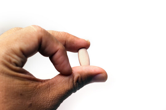 A hand holding a single light brown oval tablet against a plain white background.