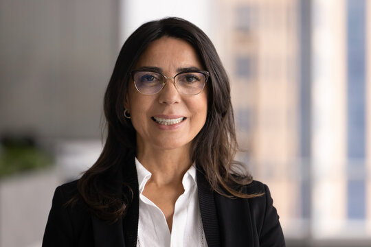 Positive middle-age female executive posing for portrait in corporate office, smiling, looking at camera, represents leadership, confidence, and professionalism. Career, business success, achievement