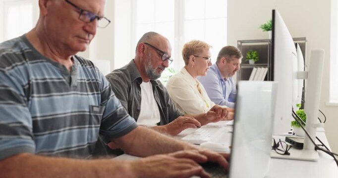 Seniors adults students in computer classroom learning. They practice typing at desktop monitors in workshop training to build skills and confidence. Concept of lifelong digital education.