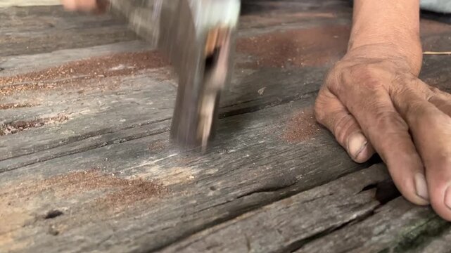 Hammering on Wood: A close-up shot captures a weathered hand skillfully using a hammer to work on an aged wooden surface, showing a craftsman's dedication.