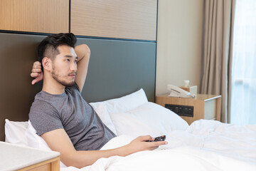 Obraz premium Man Relaxing on Bed in Hotel Room with Remote Control