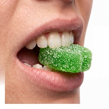 Person biting sugary green candy showing teeth for dentist warning