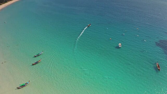 Stunning tropical beach in Phuket, Thailand, crystal clear turquoise ocean water, white sand and traditional longtail boats floating peacefully. Summer vacation travel background. Aerial top down view