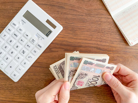 お金を数える女性の手と机上の電卓と通帳／家計管理イメージ