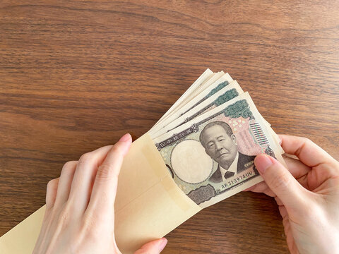 木製テーブルで茶封筒に入った紙幣を取り出す女性の手元