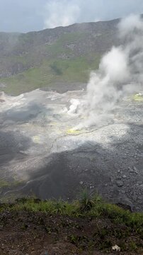 Active volcanic crater with sulfur steam vents and green mountain slopes