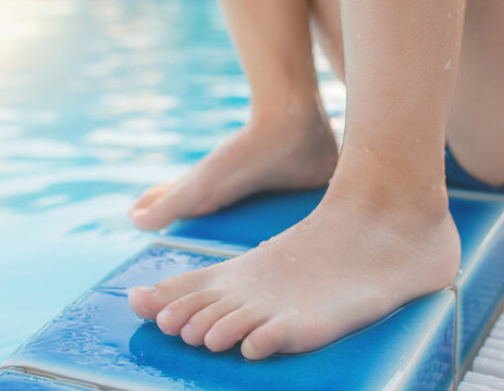 Close-up of a child's bare feet resting on the edge of a blue swimming pool.