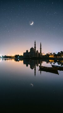 Mosque silhouette with crescent moon and reflection at night