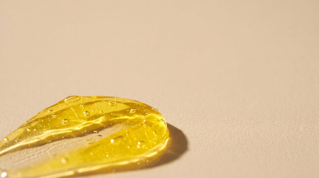 Close-up texture of golden serum or gel with small bubbles and highlights, casting a soft shadow on a neutral beige background, cosmetic product sample, skincare