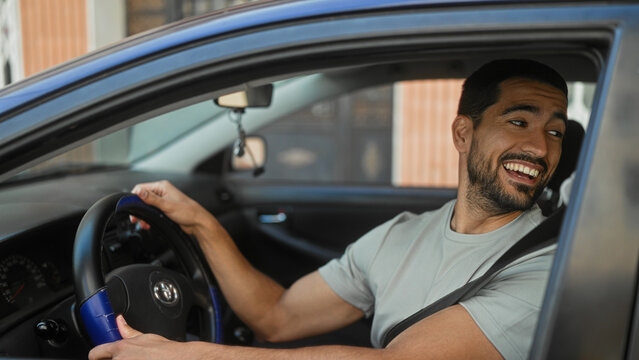 Man at steering wheel with hand on wheel turning head and reaching for rearview mirror on street; casual friendly moment.