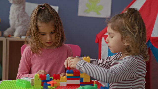 Girl arranging colorful plastic blocks with hands at a play table in a building; quiet concentration.