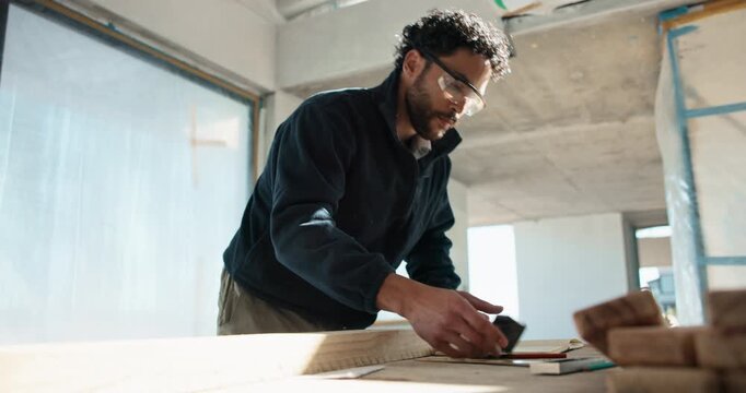 Carpenter, man and writing with notebook for home renovation, craftsman checklist and blow sawdust. Person, project and woodwork in house with remodeling, plan and carpentry notes for construction.