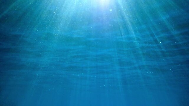 Underwater background with clear blue ocean water, bright sun rays beaming through surface and ripples, deep sea scenery. Sunlight rays shining. Waving sea water surface underwater view. Real video.