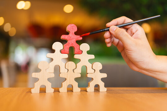 Leadership and talent recruitment concept with hand painting top wooden figure in red on human pyramid structure on table for career promotion, business success and individuality.