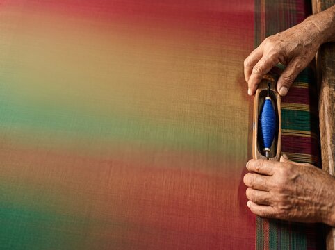 Artisan hands weaving colorful fabric on a loom with blue thread.