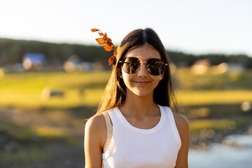A girl stands by a shimmering river on a bright day, wearing stylish sunglasses and a white tank top © liliyabatyrova