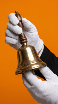 Hand in white glove holding brass service bell. Hotel service, hospitality, customer attention, restaurant service, hotel industry.
