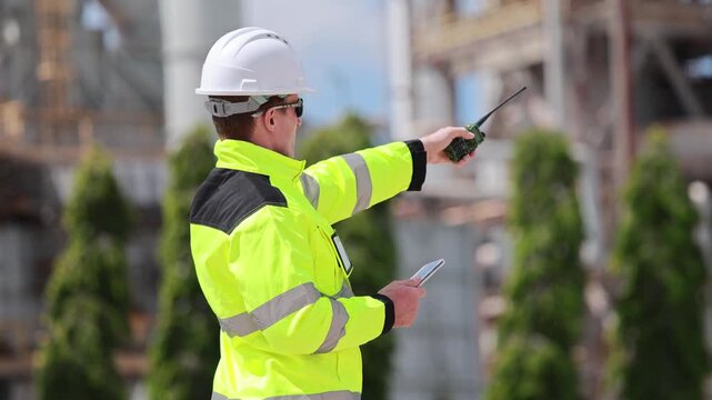 Industrial engineer in high visibility vest communicating with radio at oil and gas production plant, Worker man monitoring refinery infrastructure, Technician checking equipment at construction site