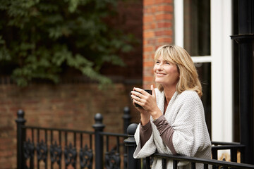 Fototapeta premium Coffee, home and thinking with happy woman on balcony for morning break, contemplation or vision. Drink, reflection and smile with mature person outdoor on terrace for memories, nostalgia or planning