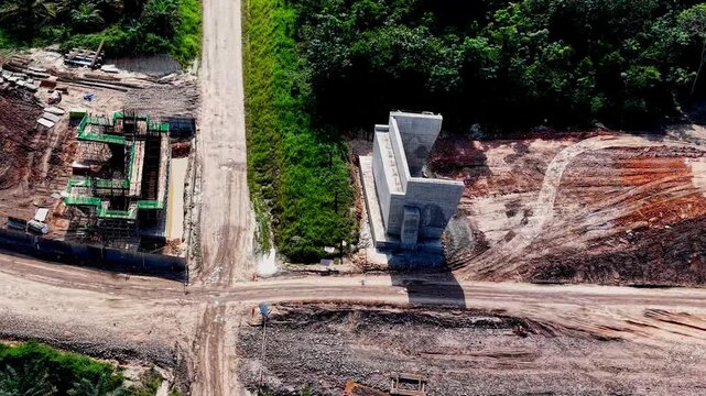 Aerial drone view of a bridge construction site featuring a massive concrete pillar and earthwork development.