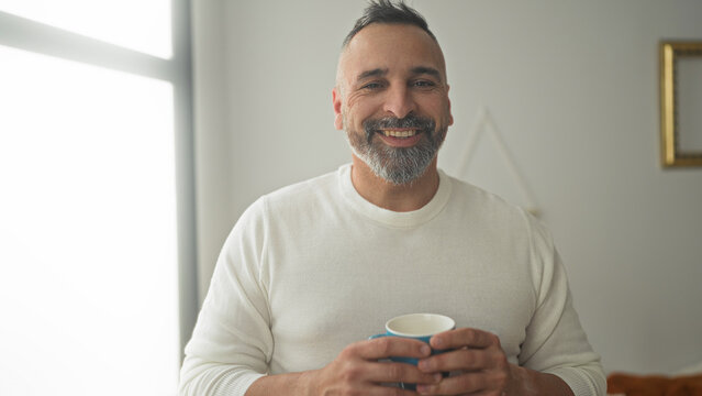 Man holding a mug with both hands, eyes closed while savoring coffee in a building; morning ritual contentment.