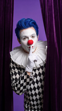 Clown peeking from behind purple curtains with finger to lips. Entertainment, performance, showbiz, theater.