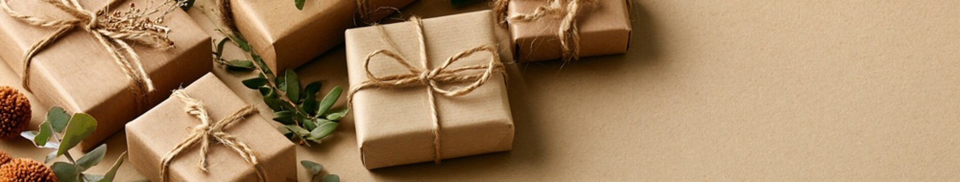 Eco friendly kraft paper gift boxes tied with jute twine, eucalyptus and dried botanicals on a neutral background