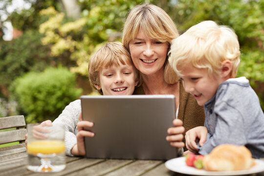 Grandmother, children and tablet outdoor with happiness for streaming, entertainment and bonding. Mature woman, boy kids or grandchildren with smile, technology and cartoon subscription with internet
