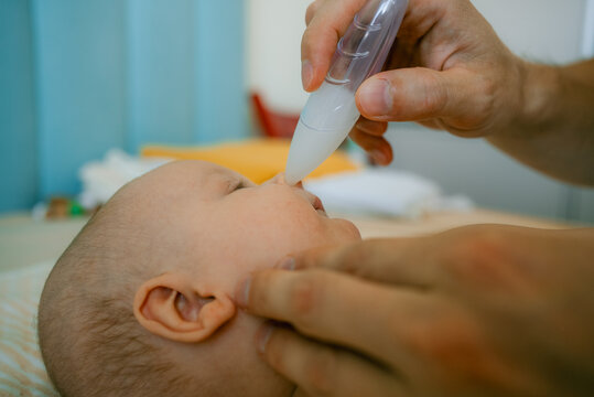 Father holding an infant on a changing table, using a nasal aspirator to clean the baby's nose, extracting mucus to clear nasal passages and assist with breathing