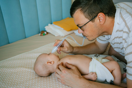 Father carefully performing nasal aspiration on a baby, clearing mucus with a specialized device to improve the infant's breathing and maintain good hygiene