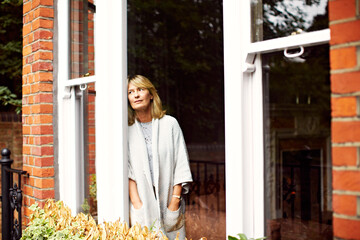 Fototapeta premium Morning, thinking and mature woman by door of home for break, relax or vision and wellness. Daydream, idea and reflection of person on terrace of apartment for memories, nostalgia or planning