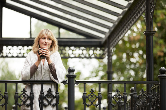 Thinking, coffee or mature woman on balcony with smile, daydreaming or nostalgia in calm mindset. Bokeh, reflection or person in house with warm drink, flashback or insight with peaceful perspective.